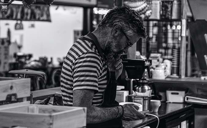 A man in a kitchen checking his phone, worried about his cancer diagnosis