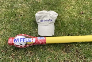 A Fans for the Cure baseball hat and a Wiffle ball and bat lying on the grass.