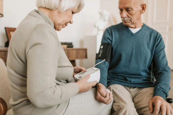 An older woman checking the blood pressure of her husband.