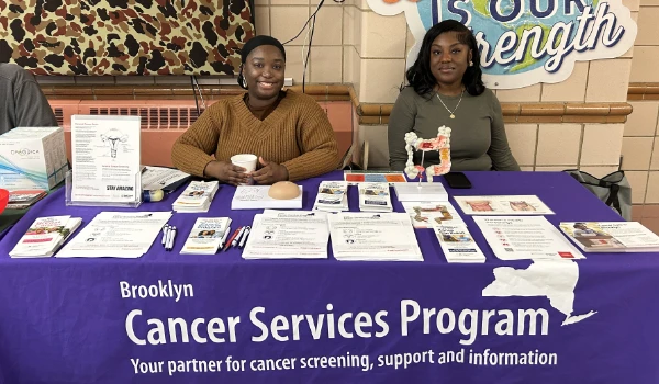 Two women sit at an information table for Brooklyn Cancer Services Program