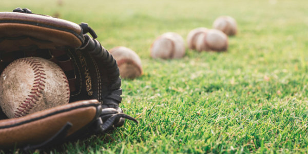 A worn mitt holding a baseball, lying on the grass, with more baseballs spread around the grass.