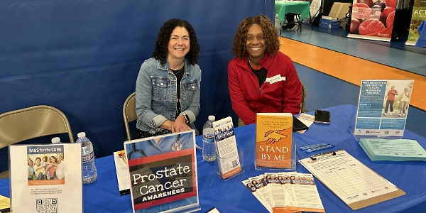 Karen Shaffer and a community health activist seated at a Fans for the Cure table at a health fair in NJ.