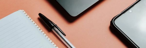 A pen next to a notebook, a phone, and a laptop