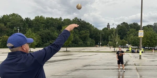 Two guys having a catch in a rainy parking lot outside the Brewers stadium.